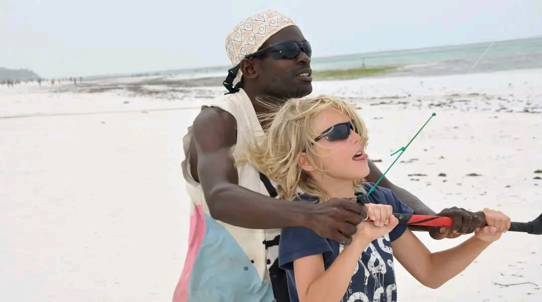 Instructor helping a young student hold the control bar on the beach