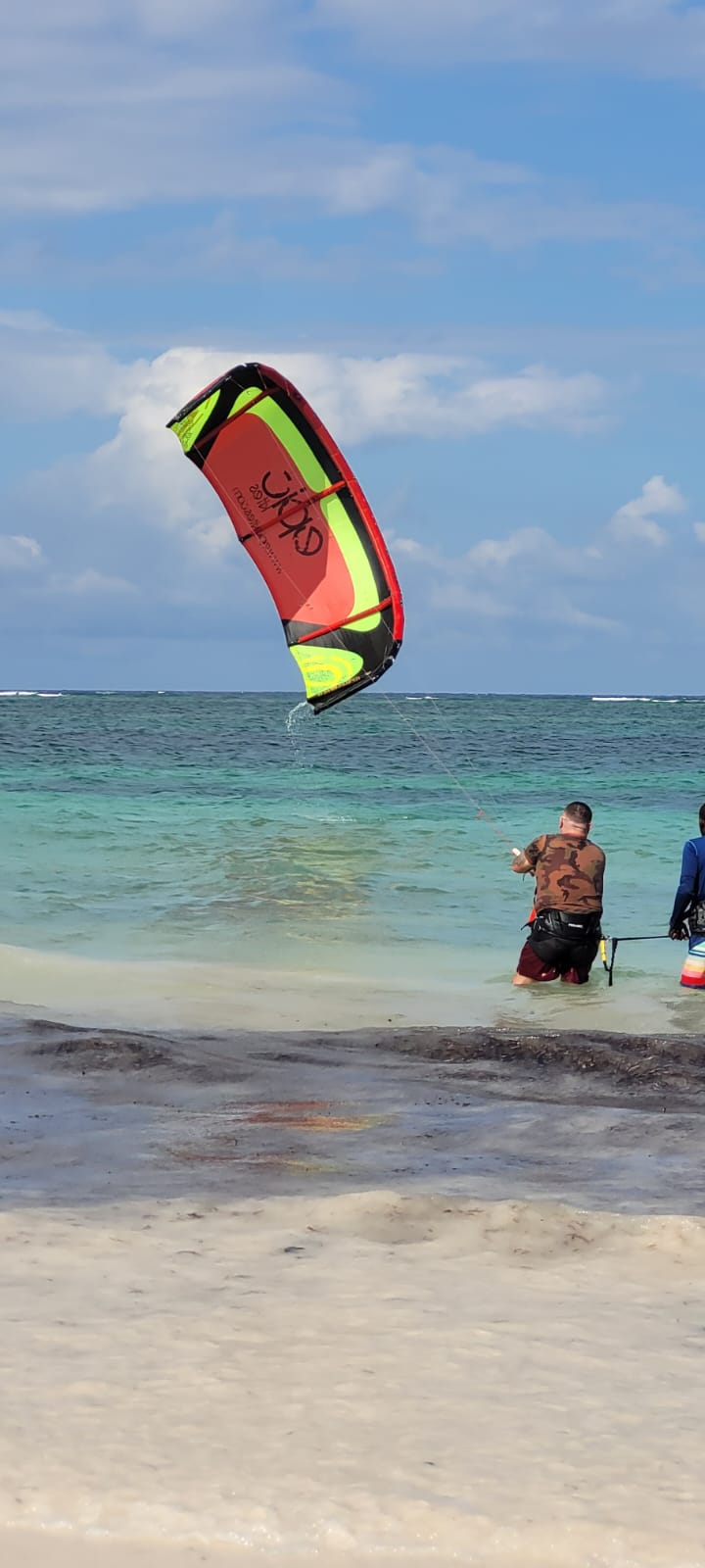 Colourful kite flying above the lagoon while riders wade out from the beach