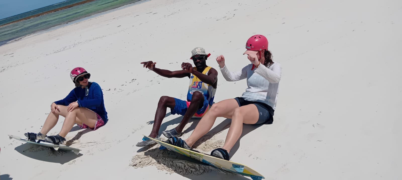 Instructor explaining board technique to two students sitting with kiteboards on the sand