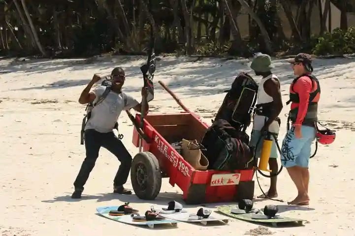Instructors preparing kites and kiteboards beside the gear cart on the sand