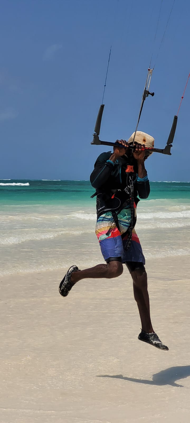 Instructor lifted off the sand by his kite in front of the turquoise lagoon