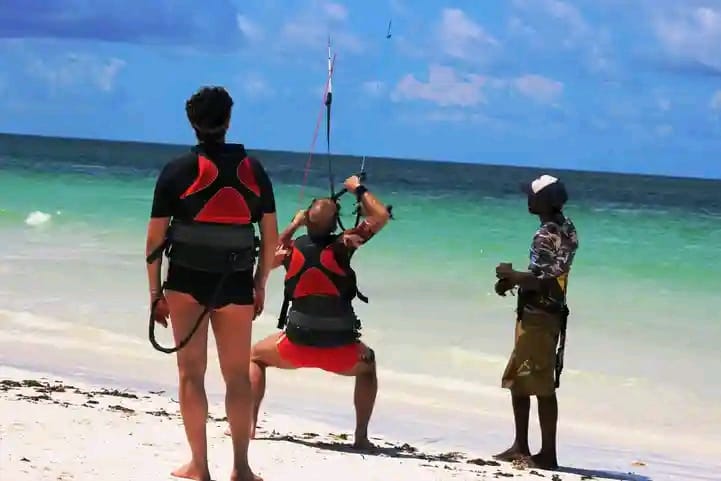 Instructor briefing two students in harnesses at the water's edge